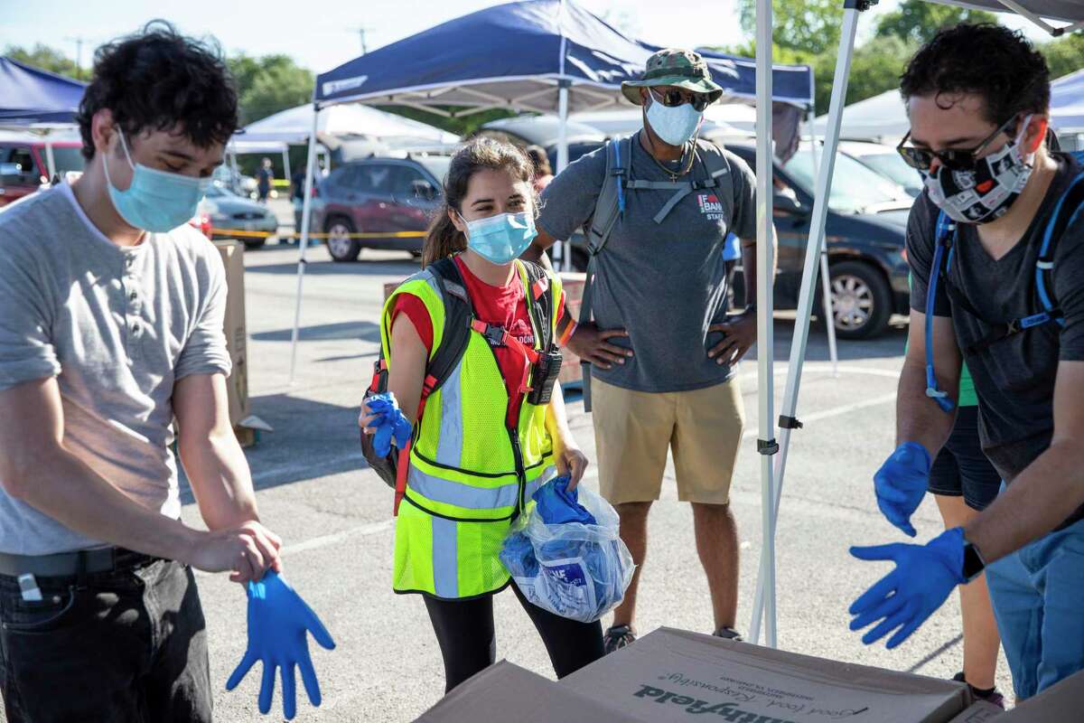 Brittany Jones, second left, passes out latex gloves to volunteers during a food distribution by the San Antonio Food Bank at the Alamodome in San Antonio, Texas, U.S, on Friday, May 1, 2020. Jones, a San Antonio native who graduated from Texas A&M at College Station, joined AmeriCorps to work with the San Antonio Food Bank where she has been organizing and distributing food to those in need during the coronavirus global pandemic.