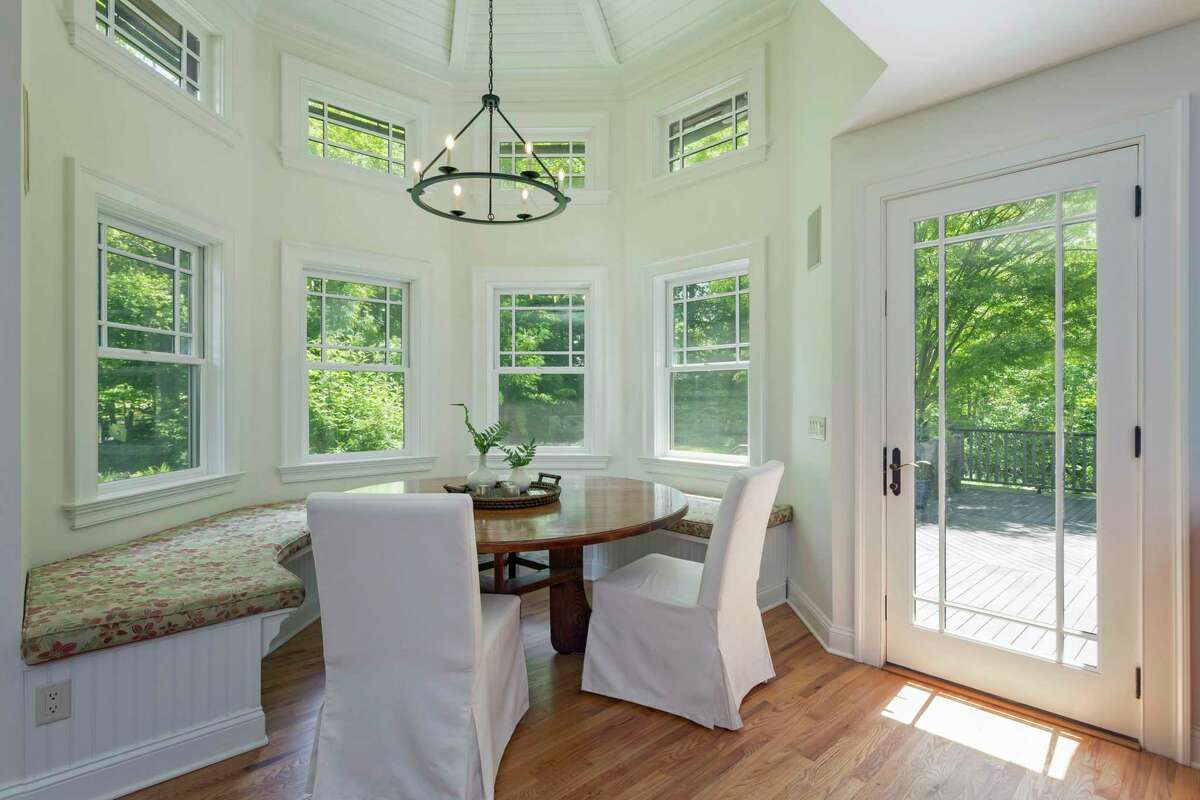 The casual dining area features a semi-circular built-in banquette, two-story windows, and a door to a raised wood deck.