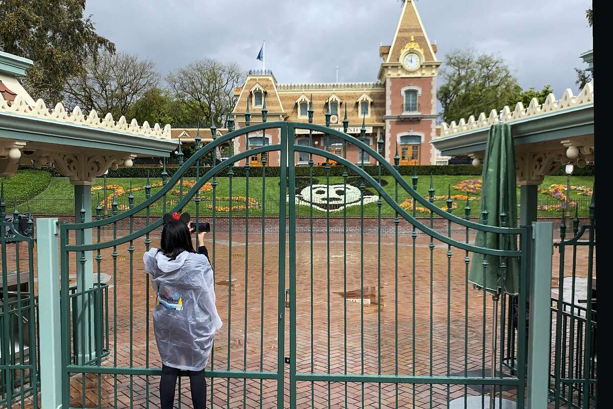 FILE - In this March 16, 2020, file photo, a visitor to Disneyland in Anaheim, Calif., takes a photo through a locked gate at the entrance. Disneyland has been shut down due to the novel coronavirus outbreak.