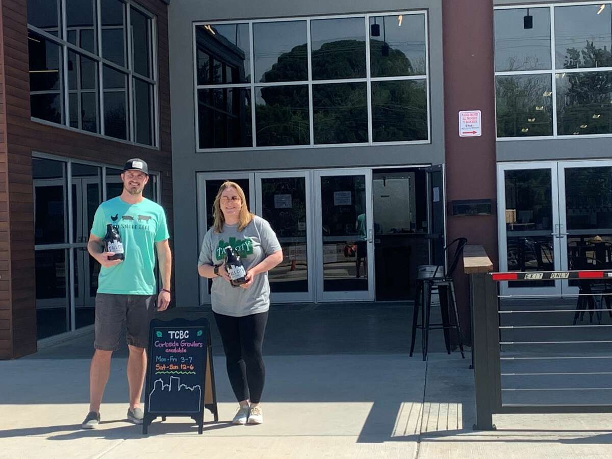 Jeff Thomas, left, and Kellyn Heck hold growlers filled with beer as they wait outside the doors of Tall City Brewing Co. to serve customers pulling into the business for curbside service. Thomas, co-owner of Tall City Brewing Co., said the curbside service has been a success with customers looking to get growlers filled with their favorite brews.