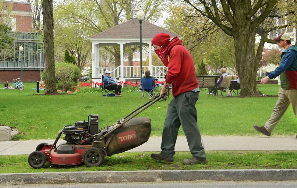 Times Union photographers capture life in the Capital Region during the coronavirus pandemic. Click through to see scenes from the crisis. A man wears a bandana on his face as he mows the grass at Glens Falls City Park on Thursday, May 7, 2020 in Glens Falls, N.Y. People are seen spaced accordingly as they socialize in the background. (Lori Van Buren/Times Union)