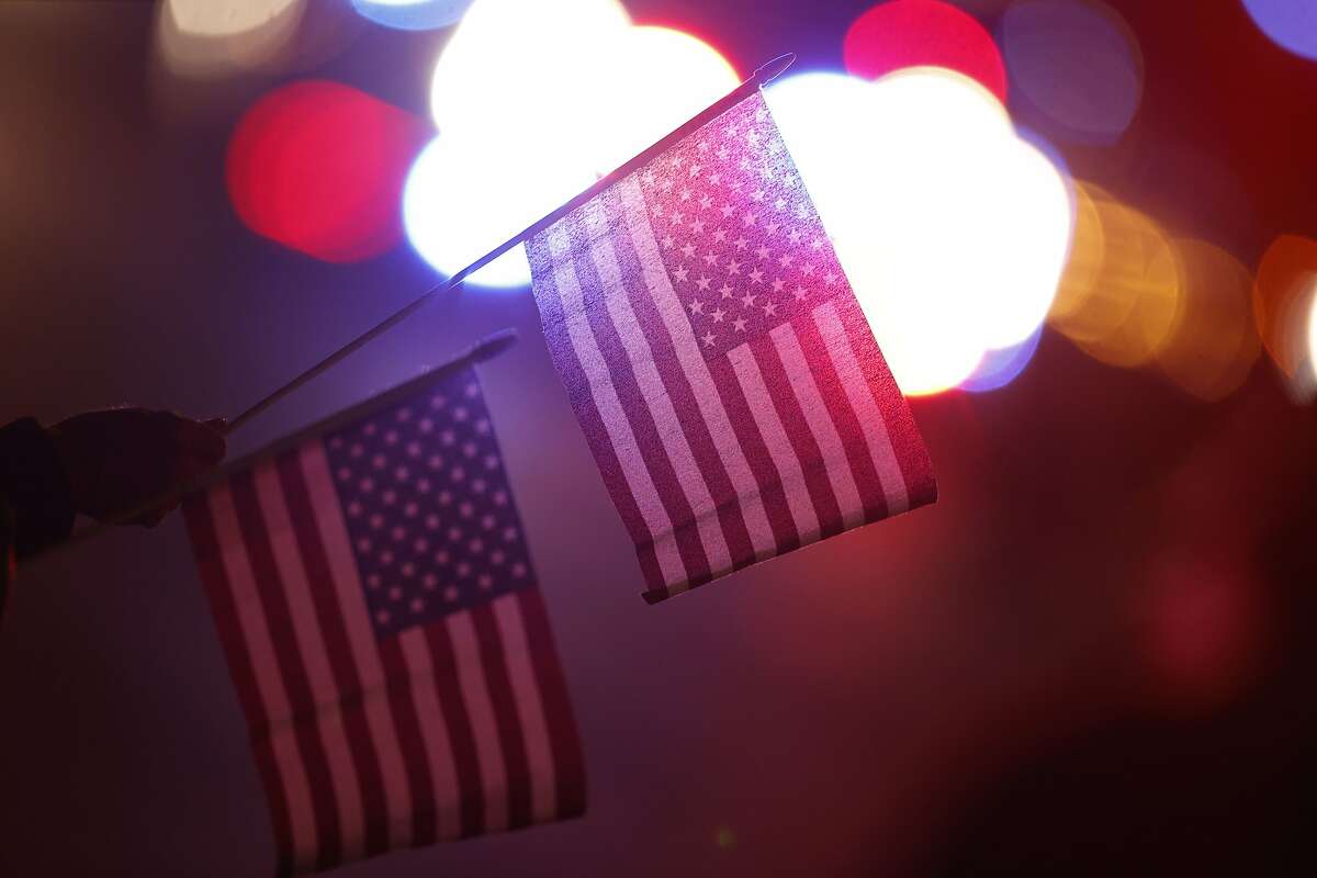 A bystander holds a pair of American flags as a large procession of emergency vehicles follows the ambulance carrying the body of retired paramedic Paul Cary late Sunday, May 3, 2020, in Denver. Cary died from coronavirus after volunteering to help combat the pandemic in New York City. (AP Photo/David Zalubowski)
