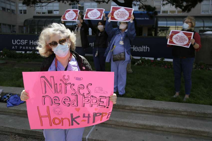 Operating room nurse Jennifer Lee, left, and other nurses hold up signs at honking motorists during a May Day action demanding better COVID-19 protections for nurses outside the Parnassus campus of the UCSF Medical Center Friday, May 1, 2020, in San Francisco. The May Day actions by nurses were taking place at 139 hospitals in 13 states Friday.