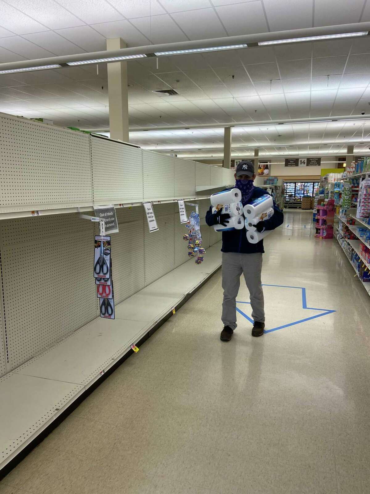 A masked customer is stocking up on needed paper supplies amid the nearly empty supermarket shelves.