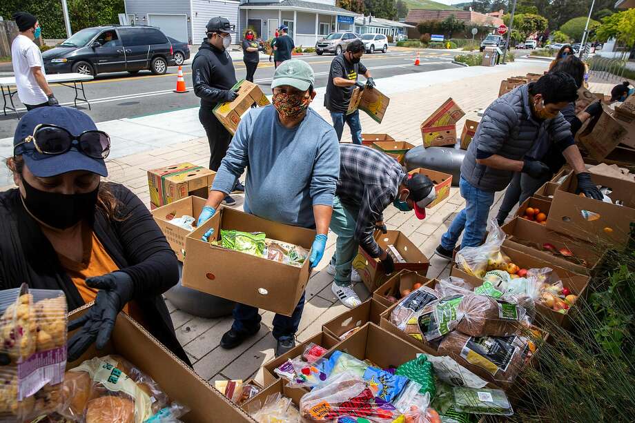 左起:志愿者胡安娜·鲁诺和胡里奥·洛佩兹接受捐赠的食物，这些捐赠将于2020年5月2日星期六在加利福尼亚州半月湾的一个临时汽车餐厅组织并分发给需要的人。在冠状病毒大流行期间，有需要的人在没有离开他们的车的情况下就收到了一盒食物和礼品卡。该活动由Ayudando Latinos A So-ar (ALAS)主办。ALAS是半月湾的拉丁文化艺术和社会服务项目。图片来源:Santiago Mejia / The Chronicle