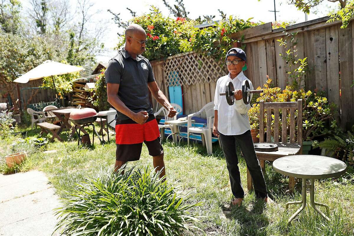 Jason Gittens encourages his son, Kekoa, 9, as he does curls as the PE portion of his virtual school day at their residence in San Rafael, Calif., on Wednesday, May 6, 2020. Gittens ia gaffer and cameraman that has had his work totally dry up during pandemic and ensuing shelter in place.