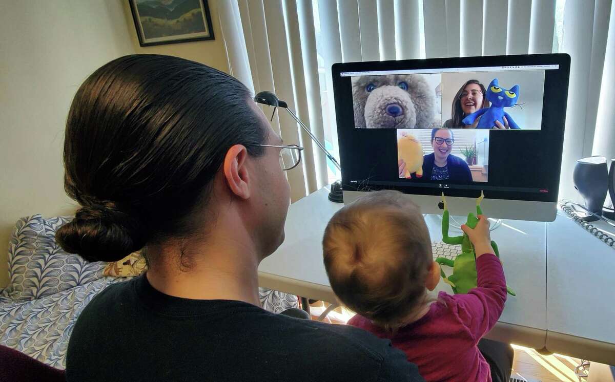 Thomas and Aurelia Kozak, 14 months, watching Stuffed Animal Picnic Storytime. The Youth Services librarians on screen are Anna Taylor (teddy bear), Kaitlin Frick (blue cat), and Samantha Cardone (yellow pony).