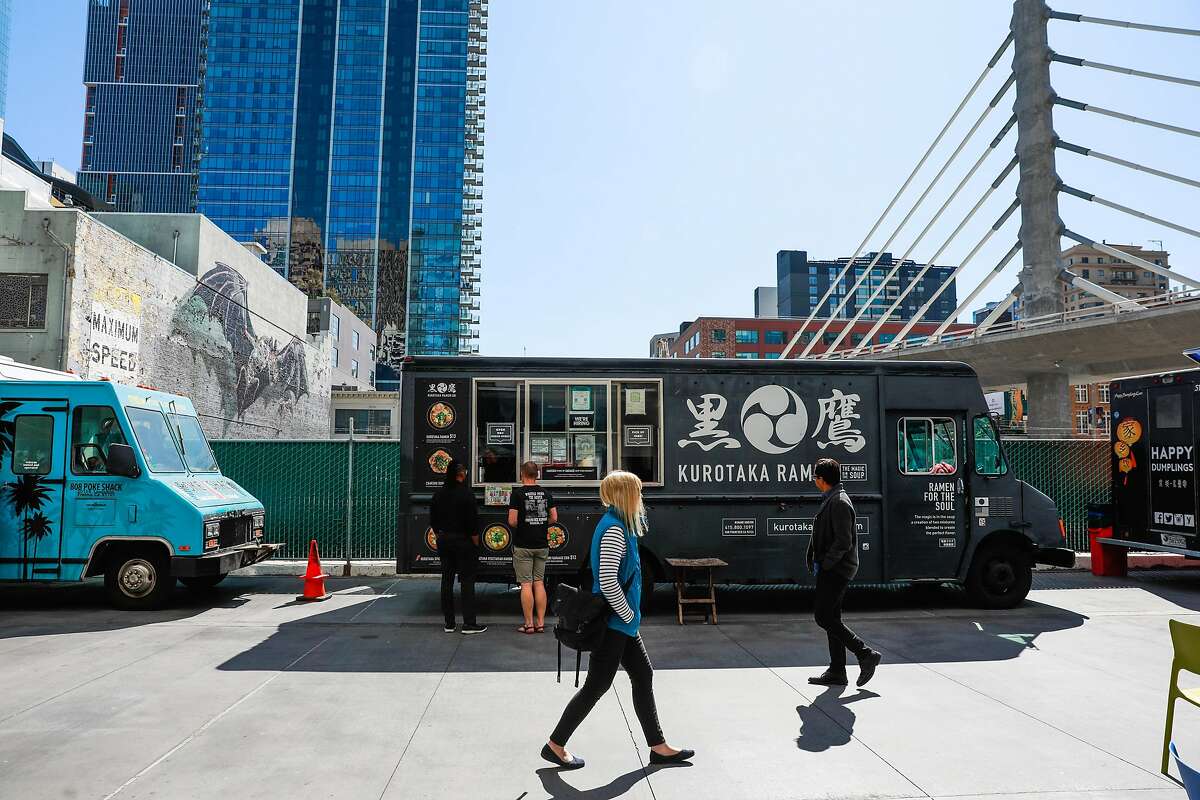 People walk past food trucks for lunch outside the Transbay Terminal on Wednesday, March 11, 2020 in San Francisco, California. Despite dozens of people coming out for lunch, it was much quieter than normal due to many people working from home because of the coronavirus.