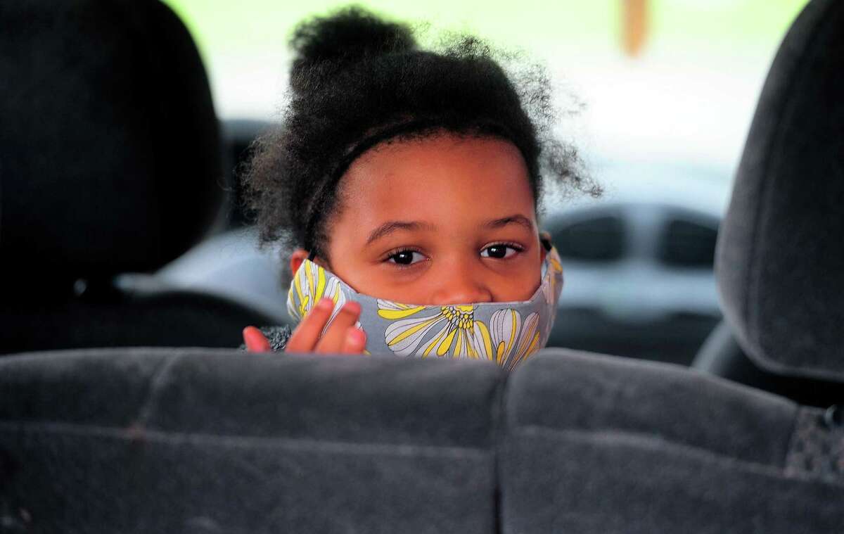 New Beginnings Family Academy student Zamea Lewis, 7, waits in the back seat for a laptop to be dropped off to her during a laptop giveaway at the school in Bridgeport, Conn., on Friday May 1, 2020. Local charter schools were shut out of the school district's free computer distribution, but New Beginnings donors stepped up, letting the school provide several hundred laptops to their students.