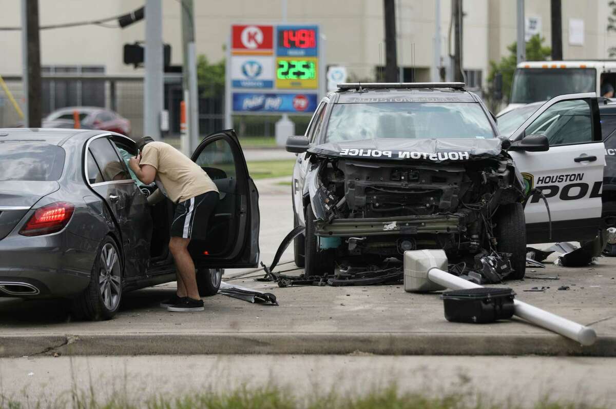 A man looks into a vehicle at the scene where a police cruiser and that vehicle collided during a police pursuit Tuesday, May 12, 2020, in Houston. The driver being pursued, in another vehicle, fled to a nearby home, and officers apprehended him after a short foot chase.