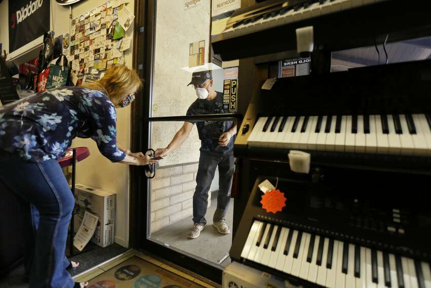 Michael Chin, right, with the band Midnight Crush, purchases guitar strings from Diane Shibley at the Napa Music Supply store, Friday, May 8, 2020, in Napa, Calif. Some California retailers and manufacturers were able to reopen Friday under a new plan by Gov. Gavin Newsom aimed at easing the state's stay-at-home coronavirus order. His plan released Thursday allows some counties to go further by opening restaurants for dining, but only if the counties can meet strict thresholds.