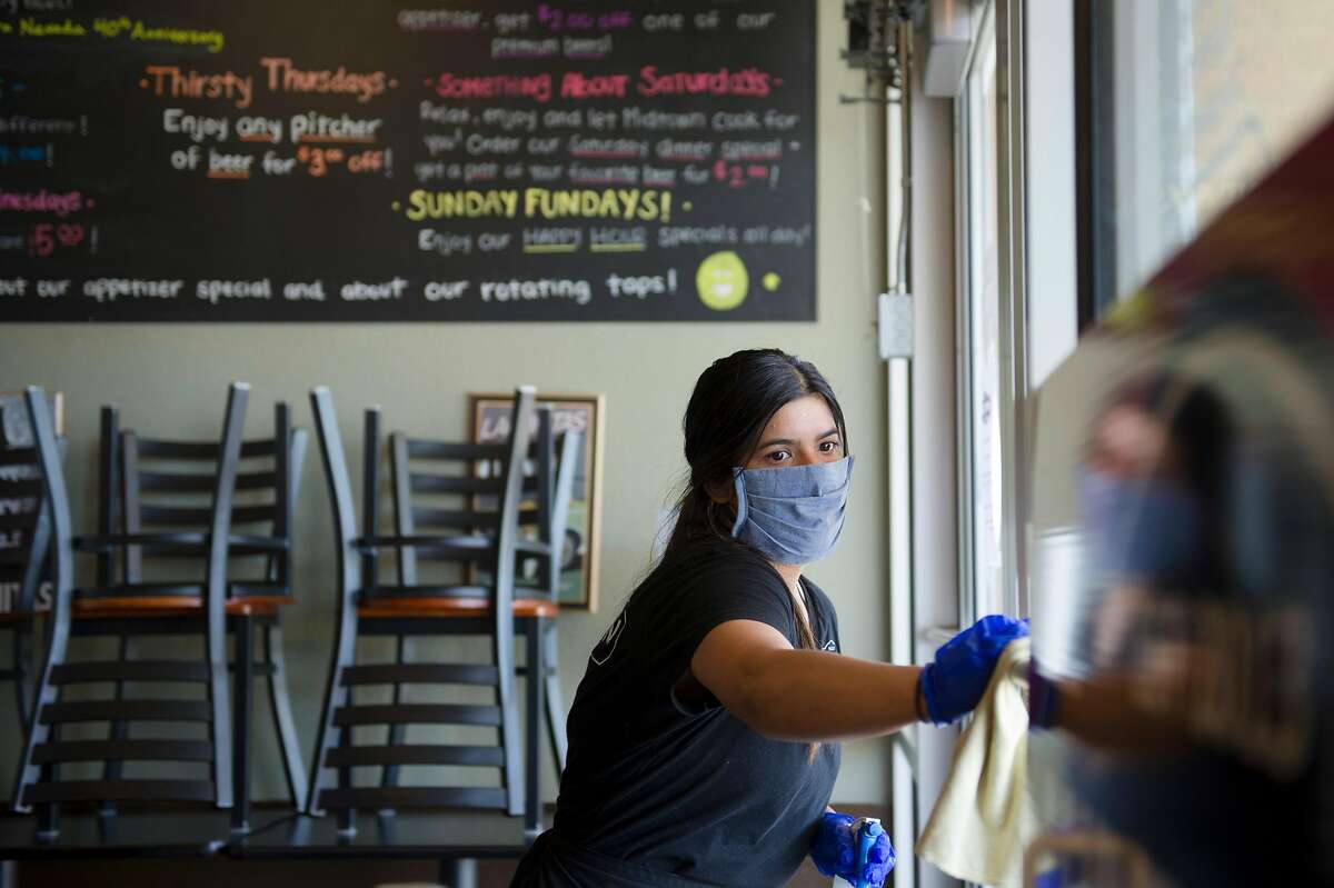 Server Alexis Quirarte of Yuba City sanitizes the front door before opening Midtown Grill in Yuba City, Calif. on Wednesday, May 6, 2020.