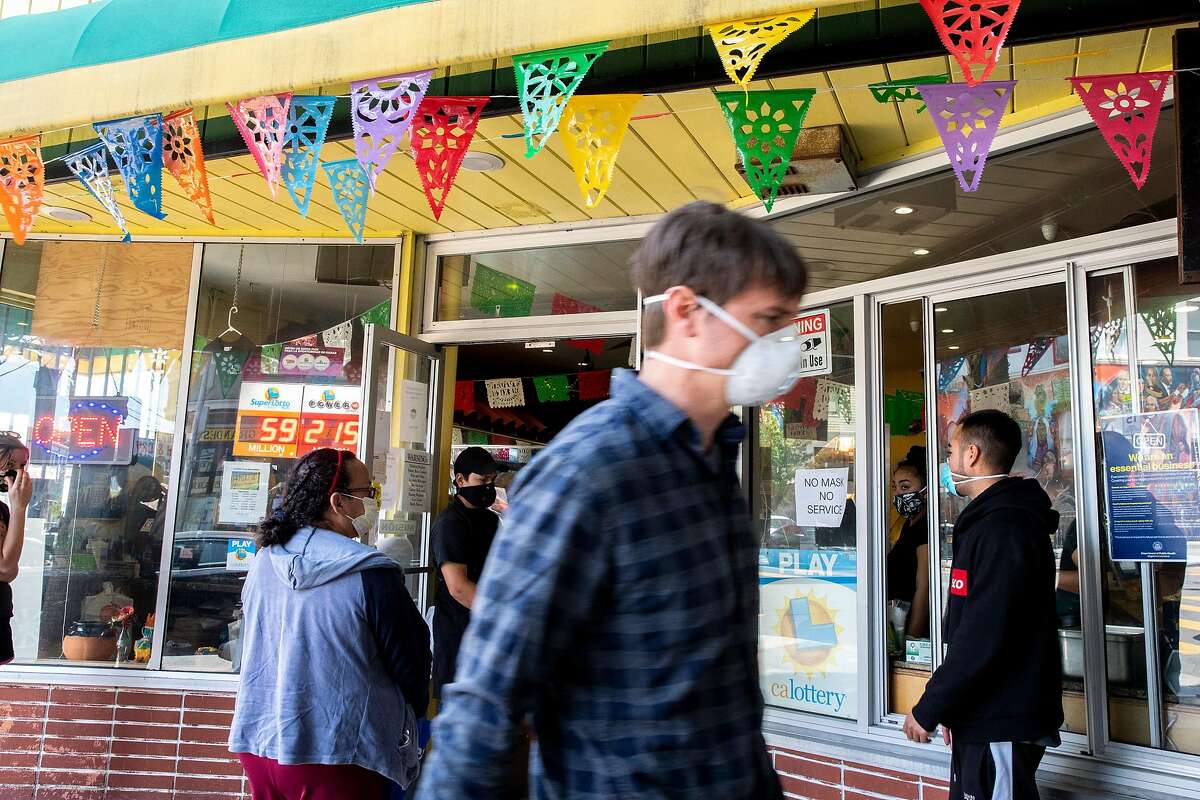 Customers wait in a social distance line to enter La Palma Mexicatessen along 24th Street on Thursday, May 7, 2020, in San Francisco, Calif. Amid the coronavirus pandemic, the business refuses to serve anyone without a mask. The food market also discourages customers from touching any merchandise if they do not intent to buy it.