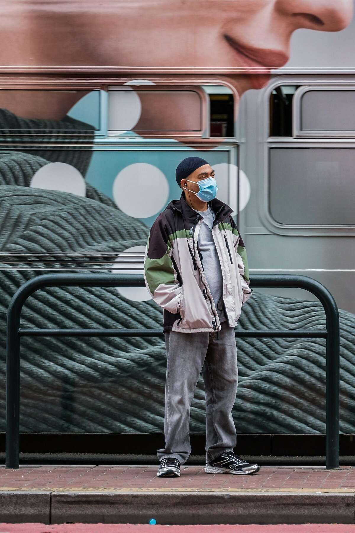 A passenger waits for a bus while another bus passes behind him in San Francisco, Calif. on Thursday April 16, 2020.