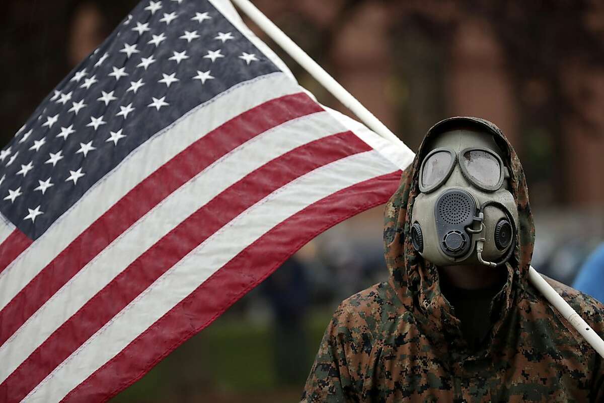 A protester wears a gas mask and carries an American flag during a rally in response to Michigan’s coronavirus stay-at-home order at the State Capitol in Lansing, Mich., Thursday, May 14, 2020. (AP Photo/Paul Sancya)