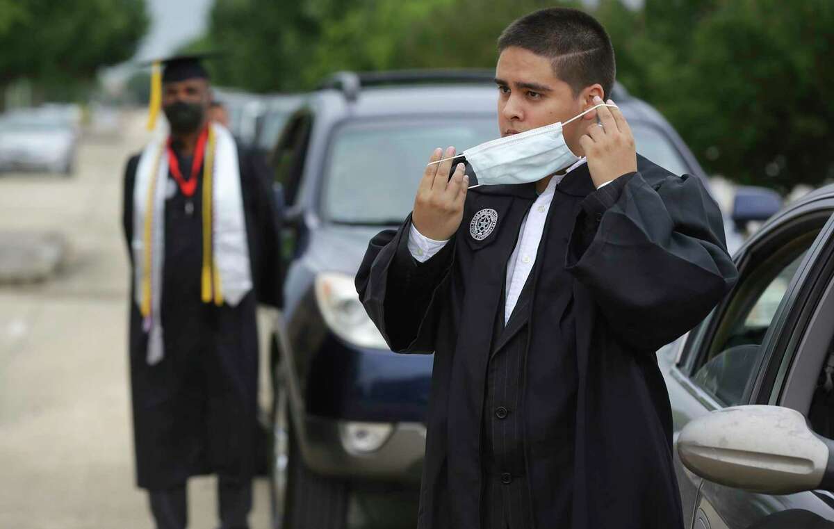 Giovanni Ramirez, right, puts on his mask as he and fellow graduate Larry Mosley, left, wait by their cars during the curbside graduation ceremony at Texas A&M University San Antonio on May 15.
