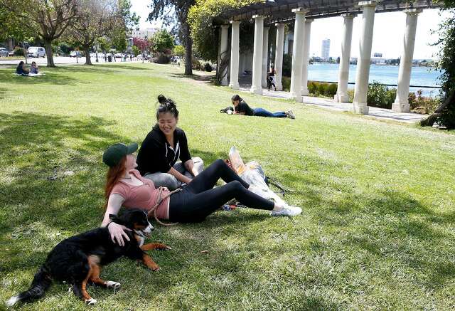 Sammy Consani and Nutella (left) sits with Hannah Suh at Lake Merritt in Oakland this month. Oakland city officials are strongly discouraging gatherings at the lake and at parks and are reminding people to maintain social distancing during the coronavirus shelter in place orders.