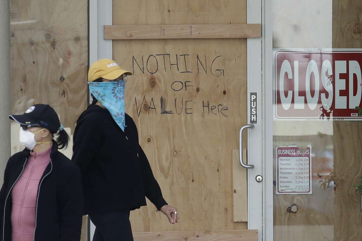 Women wear face masks while walking past a hand written sign advising that nothing of value is inside a boarded up Union Nails salon during the coronavirus outbreak in San Francisco, Tuesday, May 12, 2020.