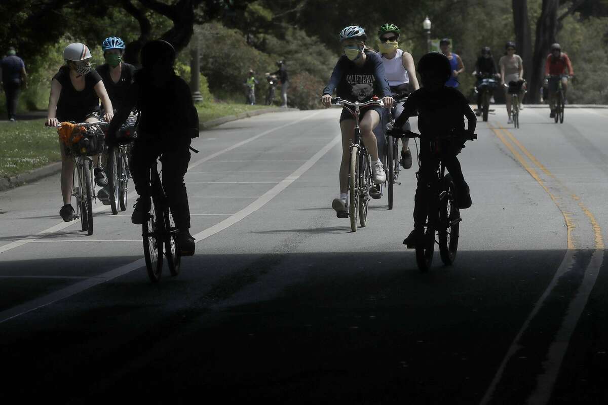 People wear face masks while bicycling on a closed street next at Golden Gate Park during the coronavirus outbreak in San Francisco, Sunday, May 17, 2020.