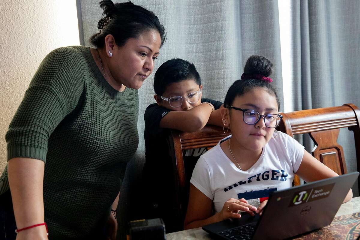 In this file photo, Oakland mother Jacqueline Perez-Rosales is checking the homework of Edgar Porcayo-Perez Jr., 10, before her daughter Montse Porcayo-Perez, 11, takes her turn on the communal laptop Jacqueline received from a nonprofit organization. The COVID-19 pandemic has uncovered not just one, but three digital divides when it comes to student learning.
