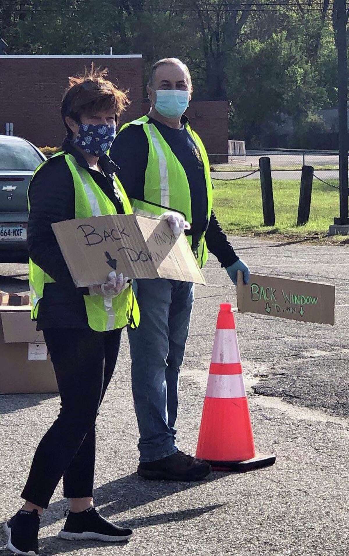 Rotarians Amy Stefanowski and Jim Hauser advise motorists to have their back window open so volunteers can safely toss into the car a bag of masks.