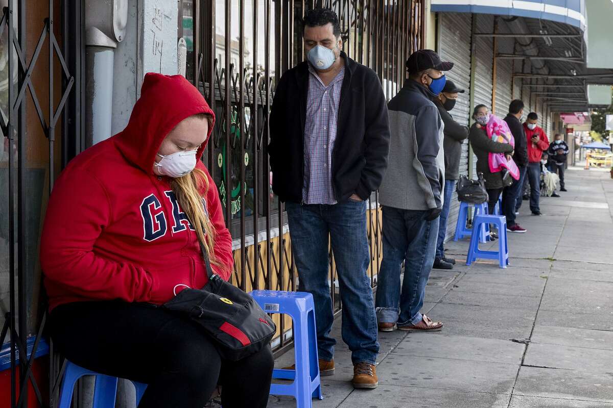 Francisco Montero (center) of Richmond wears a mask while waiting with other in a long line outside of Terra Nova Clinic in the Fruitvale neighborhood of Oakland, May 12, 2020.