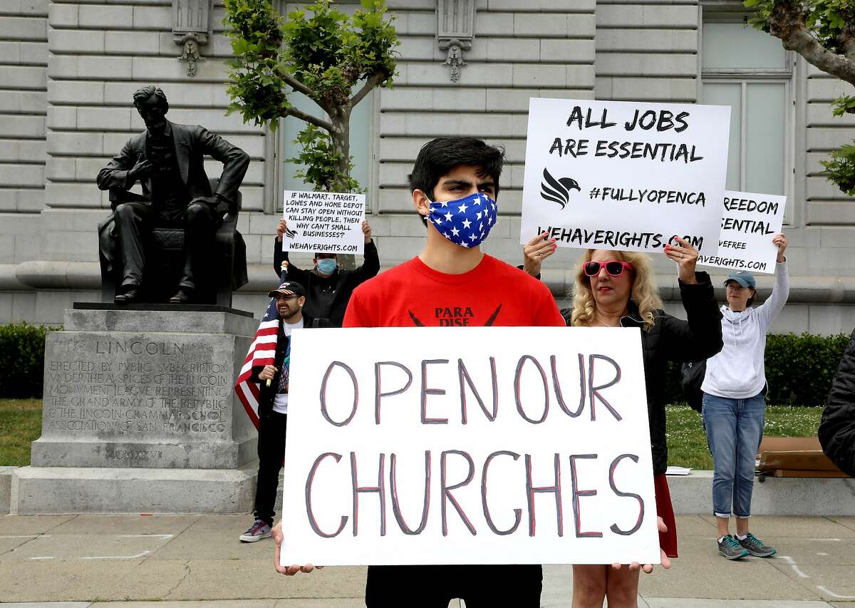 Enrique Brenes holds a sign stating, "Open Our Churches," during a rally in front of City Hall calling for Gov. Newsom to immediately reopen California completely in San Francisco, Calif., on Saturday, May 9, 2020. Protesters argued they've been stripped of their rights.
