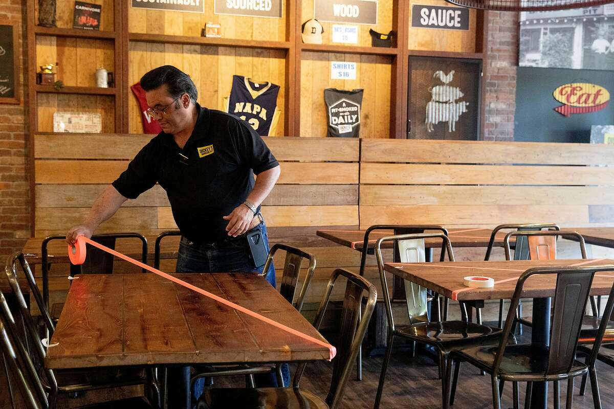 Dickey's Barbecue Pit owner Rene Bassett places tape on tables after customers asked to dine indoors at his restaurant in Napa, Calif. Tuesday, May 5, 2020. Bassett planned to open his restaurant to in-house and outdoor seating Tuesday but his plans were put on pause by the local health inspector.