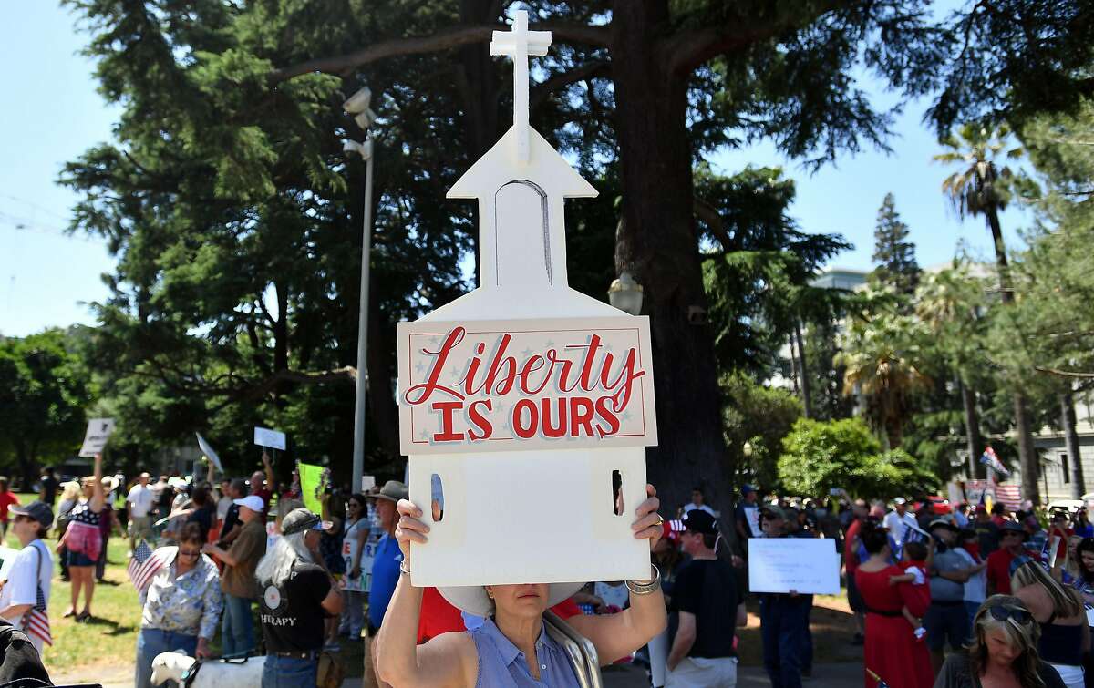 A woman holds up a sign depicting a church as hundreds of people gather to protest the stay-at-home orders outside the state capitol building in Sacramento, California on May 01, 2020. - Some people intentionally jammed roads while honking and holding out signs while others disrespected social distancing rules by gathering in close proximity, causing police to form skirmish lines to push back protesters. (Photo by Josh Edelson / AFP) (Photo by JOSH EDELSON/AFP via Getty Images)