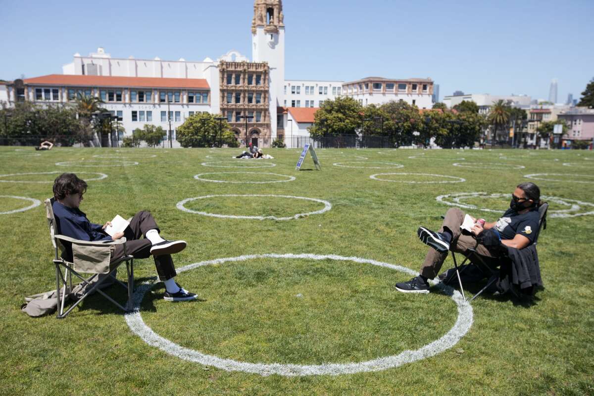 (Left to right) Steven Homer and Rahim Sharifi read books while social distancing among chalk circles in a grass field at Mission Dolores Park in San Francisco on May 20, 2020. The circles mark the required safe social distancing space required during the COVID-19 coronavirus and were created by the San Francisco Rec and Parks Dept.