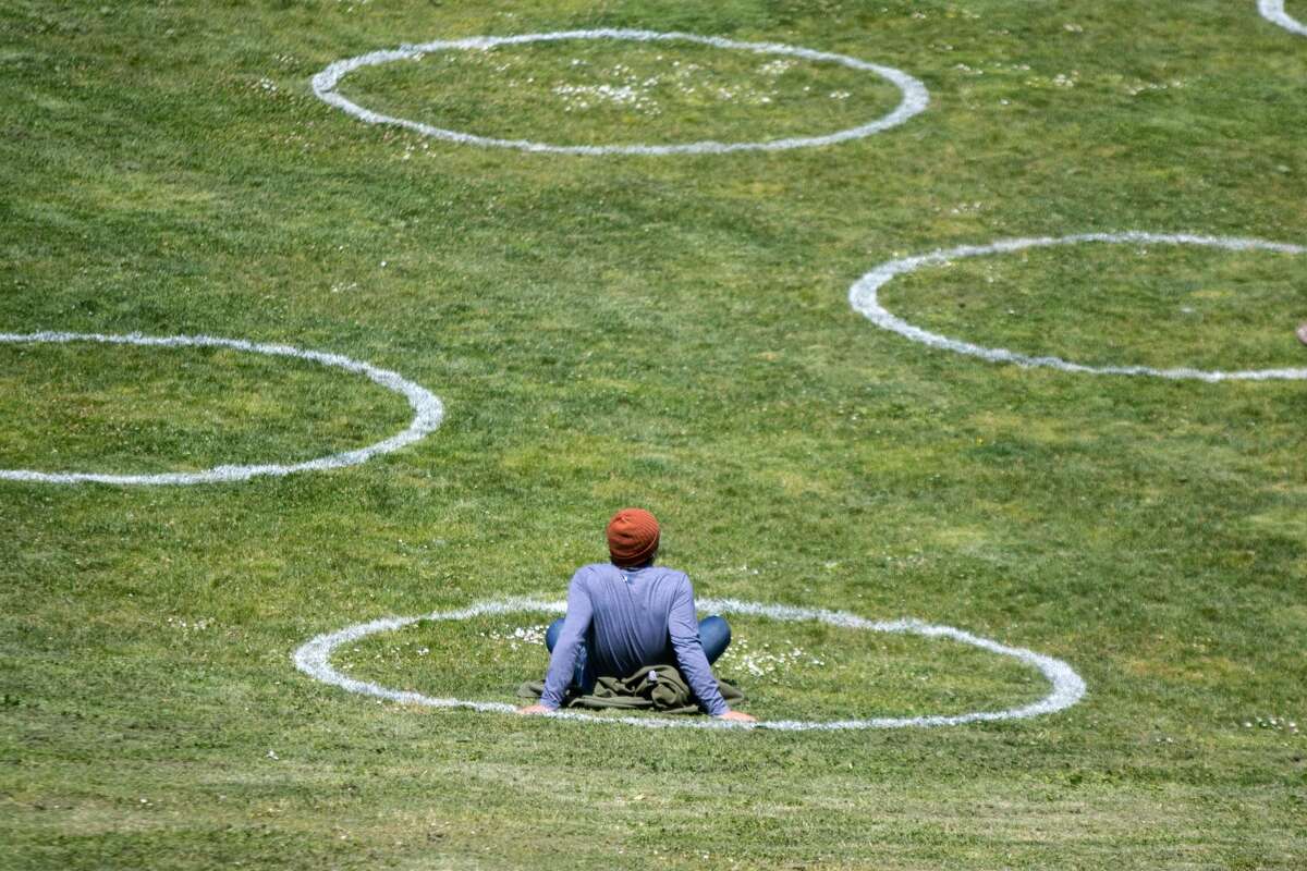 A man rests inside a social distancing chalk circles in a grass field at Mission Dolores Park in San Francisco on May 20, 2020. The circles mark the required safe social distancing space required during the COVID-19 coronavirus and were created by the San Francisco Rec and Parks Dept.