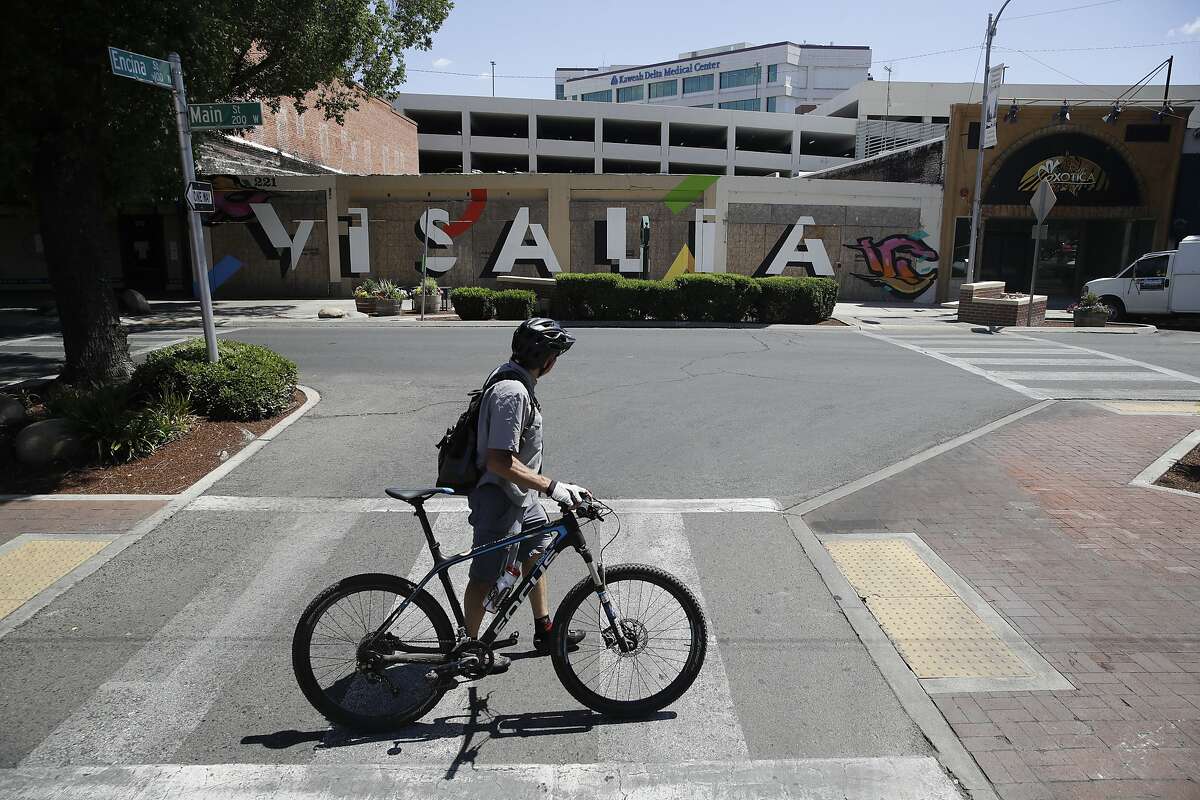 A man walks his bike past a city sign Wednesday, May 20, 2020, in Visalia, Calif. Tulare County's board of supervisors voted 3-2 Tuesday to move further into the state's four-stage reopening plan than is allowed. That means nearly all businesses and churches could reopen, though county officials said businesses should adhere to state guidelines on social distancing and other health measures. (AP Photo/Marcio Jose Sanchez)