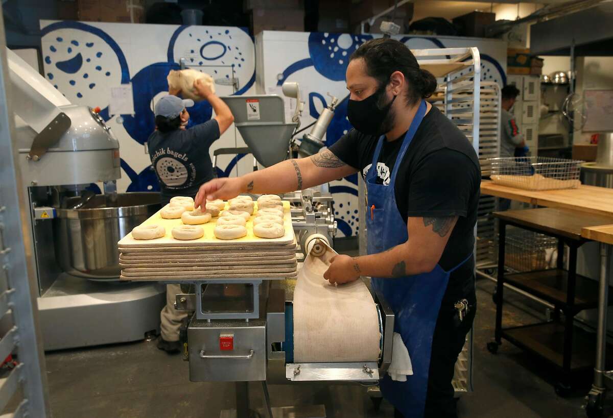 Dan Duran places bagels on a tray as Armando Carapia adds dough to a machine (background) at Boichik Bagels in Berkeley, Calif. on Wednesday, May 20, 2020. Business has remained strong at Boichik and other local bakeries during the coronavirus pandemic.