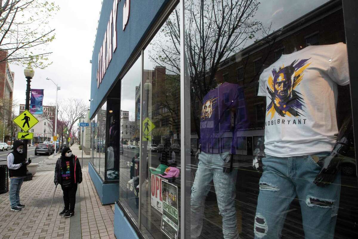 In this April 27, 2020 file photo, a couple of passersby wearing face masks walk past a closed clothing store on Main Street in downtown in Bridgeport, Conn. Connecticut lost jobs in April.