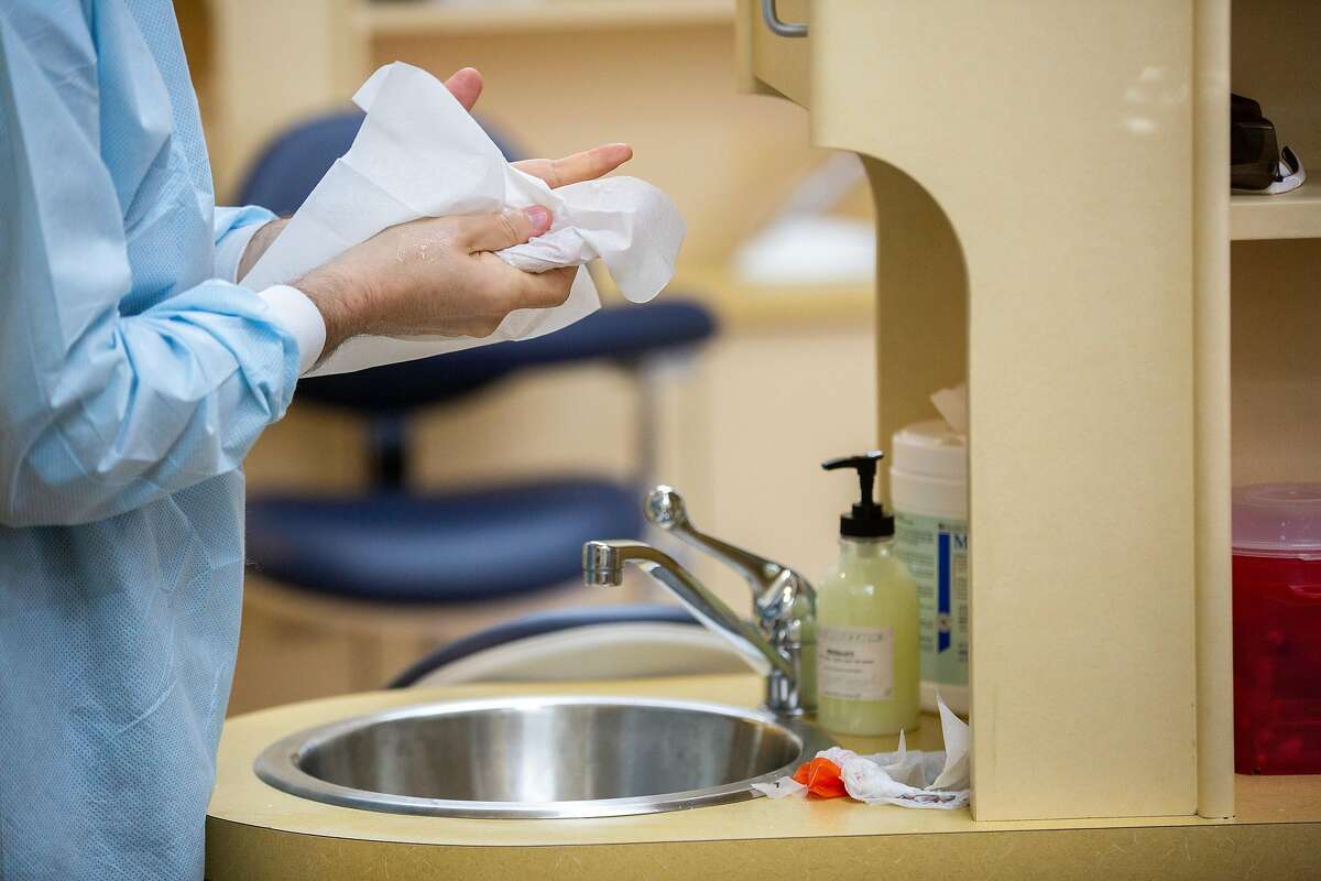 Dr. Lior Tamir washes his hands before putting on new gloves and work on a dental procedure on a patient at Bloom Dental Group on Friday, May 15, 2020, in San Mateo, Calif. The dental office has upgraded its safety, amid the coronavirus pandemic. It has several high-efficiency particulate air (HEPA) purifier and a device near the patient that continuously vacuums the surrounding air. The dentists have also upgraded their masks. They now wear N95 masks and face shields during procedures.