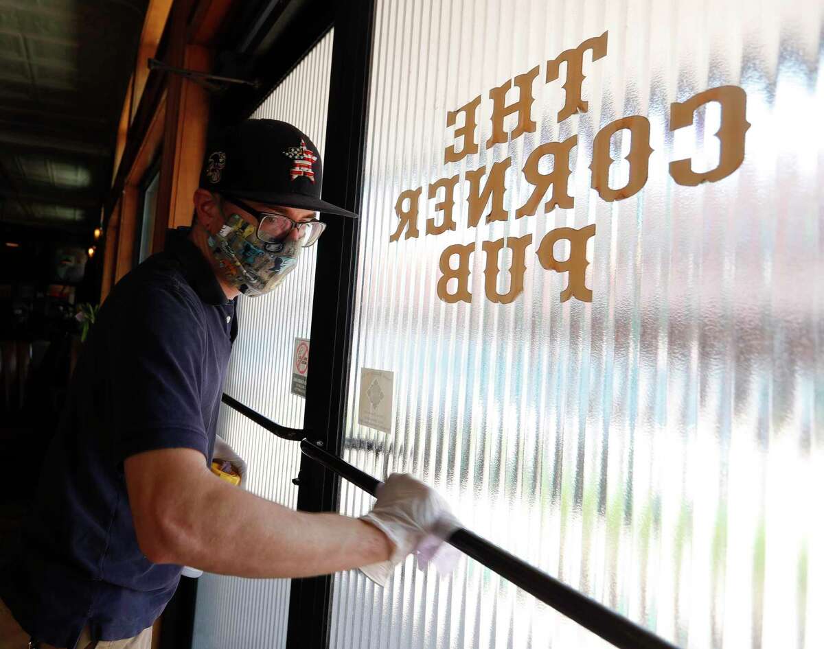 Kitchen Manager Trey Dryden disinfects door handles at The Corner Pub, Wednesday, April 20, 2020, in Conroe. The bar reopens to customers Friday with social distancing and other guidelines under Gov. Greg Abbott’s phased reopening of the economy.