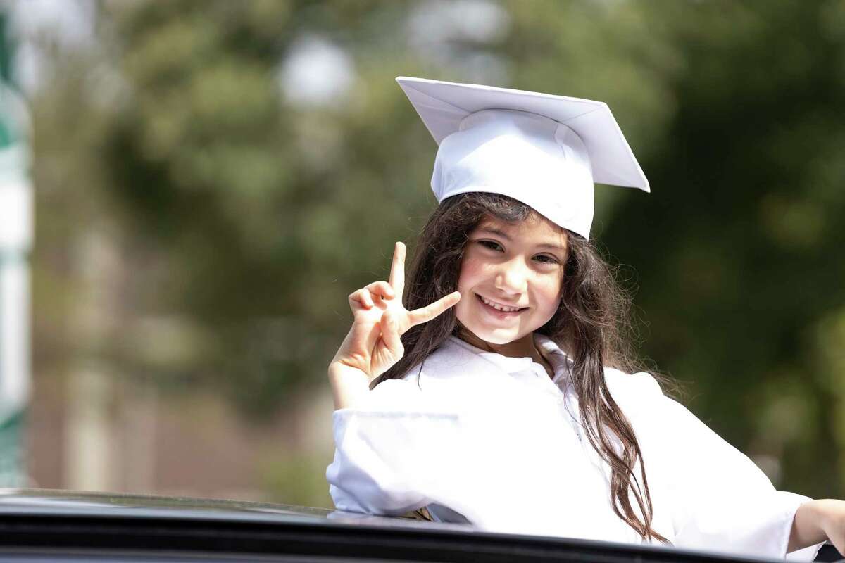 A kindergarten student throws up a peace sign during a graduation celebration at The Woodlands Christian Academy, Thursday, May 21, 2020. Around 40 students participated in the drive-by graduation ceremony where they received gifts from teachers and staff at the academy.