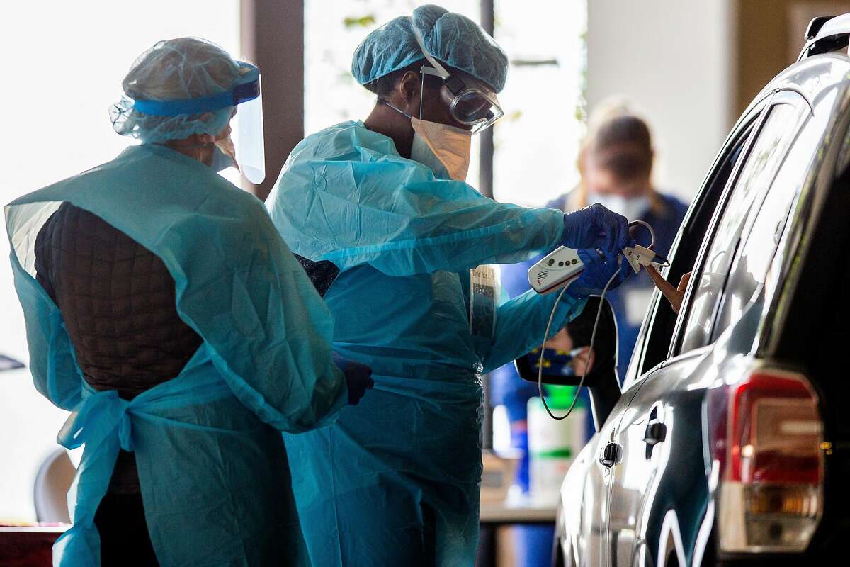 Dr. Toyin Falola (center) attends to a patient in their vehicle at the Sutter Health parking garage on Friday, April 17, 2020, in San Carlos, Calif. Sutter Health has set up 15 drive-thru care clinics in parking garages up and down the peninsula.