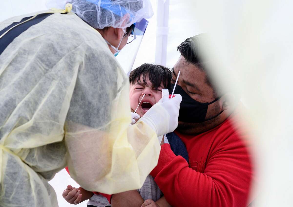 TOPSHOT - Jose Vatres (R) holds his son Aidin who reacts as nurse practitioner Alexander Panis (L) takes a nasal swab sample to test for COVID-19 at a mobile testing station in a public school parking area in Compton, California, just south of Los Angeles, on April 28, 2020. - St. John's Well Child and Family Center is providing COVID-19 testing sites in African-American and Latino communities which have been neglected in terms of testing as compared to wealthier areas of Los Angeles County. (Photo by Robyn Beck / AFP) (Photo by ROBYN BECK/AFP via Getty Images)