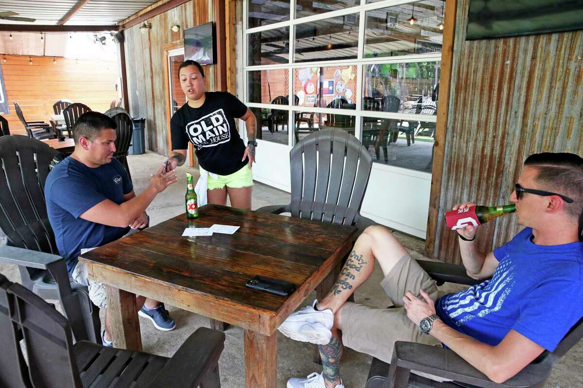 Manager Helena Herrera serves some beers to the first customers, Angel Aguilar, left, and Chris Kottke at Old Main Ice House in Cibolo.
