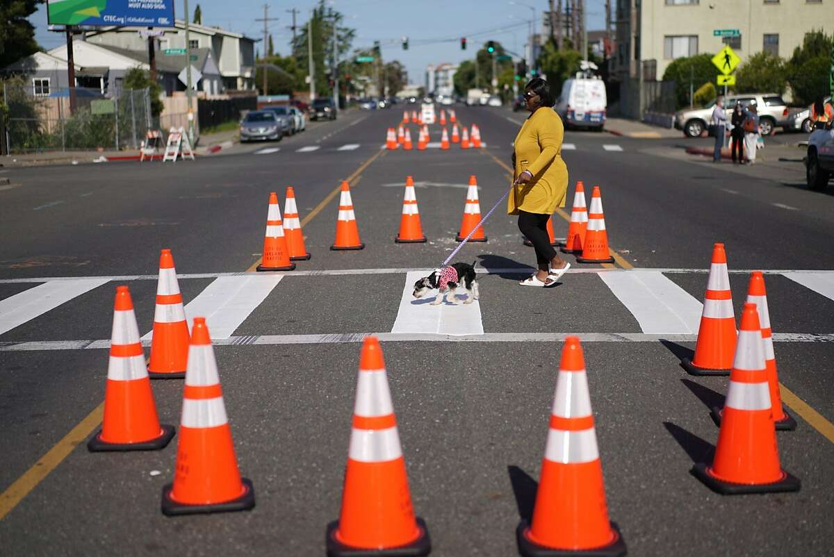 Veronica Clay with her dog �Jersey� walks among newly placed traffic cones Oakland Mayor Libby Schaaf and the Oakland Department of Transportation had placed on Bancroft Ave. for a pilot program tentatively called "Slow Streets Essential Places� on Friday, May 22, 2020, in Oakland, Calif.