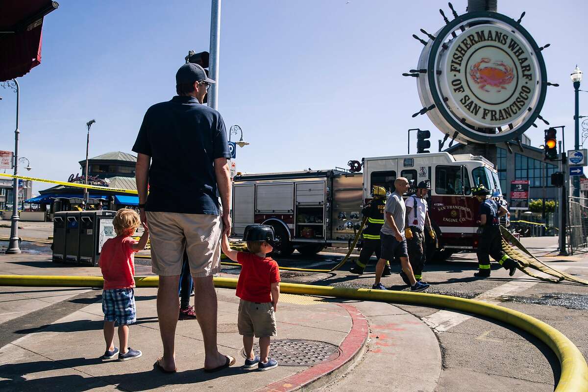 A family with a child wearing a toy firefighter hat, names declined, watch members of the San Francisco Fire Department work at the scene of a four alarm structure fire at Pier 45 in San Francisco, Calif. on Saturday, May 23, 2020.