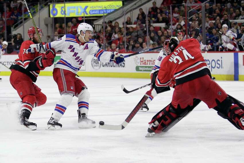 FILE - In this Nov. 7, 2019, file photo, Carolina Hurricanes goaltender Petr Mrazek (34), of the Czech Republic, blocks New York Rangers right wing Jesper Fast, of Sweden, with Hurricanes defenseman Jaccob Slavin (74) slowing Fast during the third period of an NHL hockey game in Raleigh, N.C. Carolina was one of two teams (along with Tampa Bay) that voted against the current playoff format, which doesn't reward it for being in a playoff spot when the season was paused. But the Hurricanes shouldn't need emergency goaltender David Ayres anymore with Mrazek and James Reimer healthy in net. (AP Photo/Gerry Broome, File)