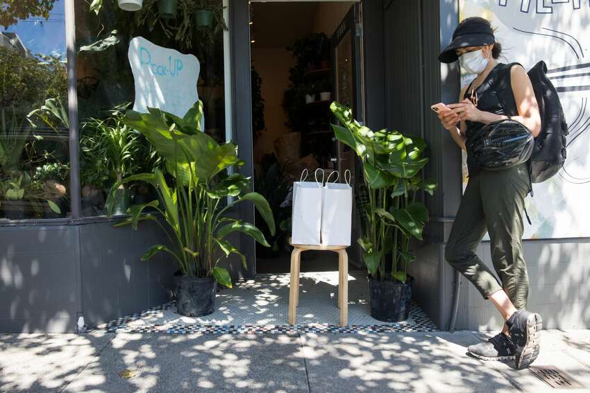 Having arrived to pick up her order, Shelley Davies uses her cell phone to buy an additional item online from Plants and Friends on Fillmore Street in San Francisco on May 27, 2020. It is one of many retail stores that have recently opened curbside or door service in San Francisco.
