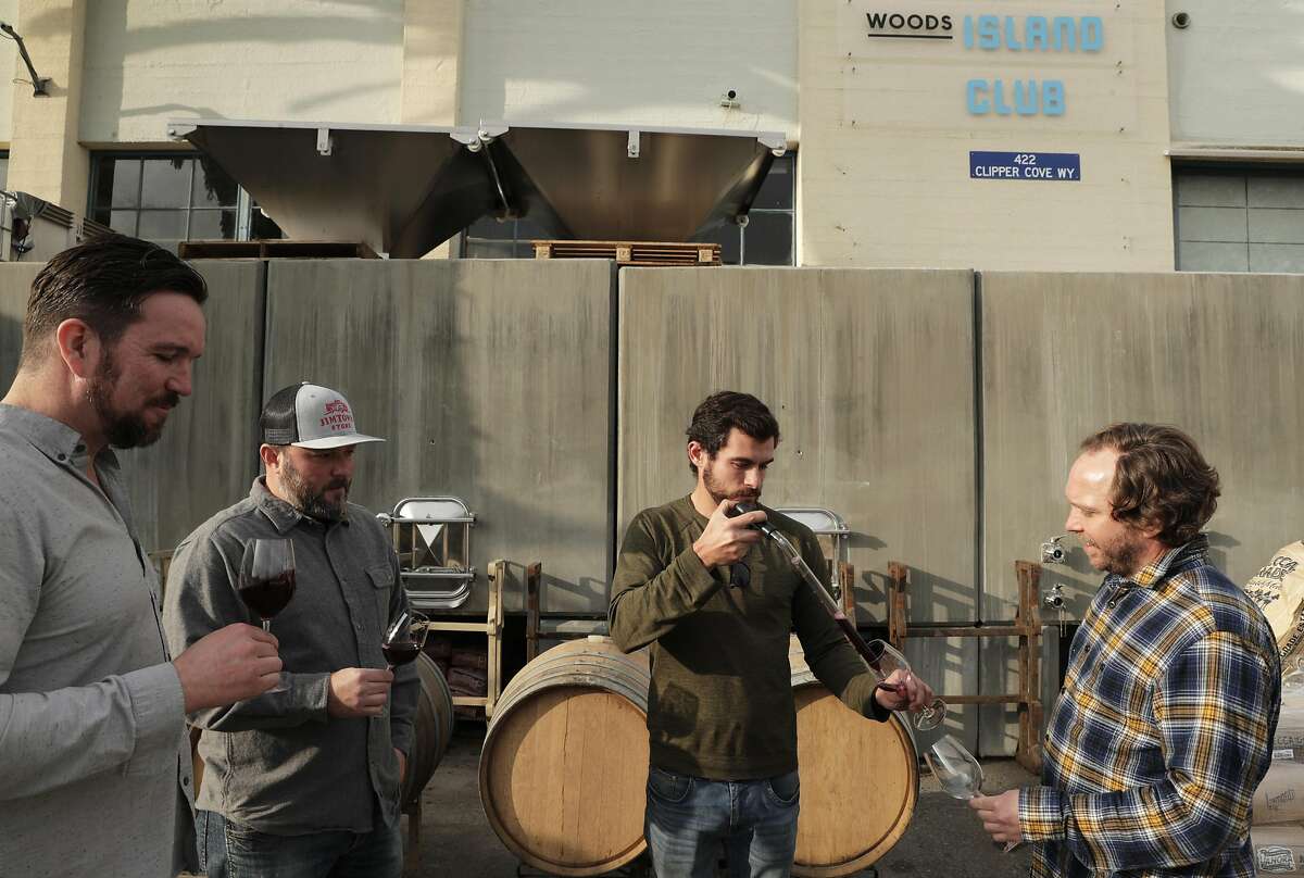 The crew at Wood's Island Club, l-r, Jim Woods, founder and CEO, Chris Scanlan, consulting winemaker, Kyle Jeffrey, assistant winemaker, and Kim Sturdavant, head brewer, in front of the concrete wine tanks at Treasure Island in San Francisco, Calif., on Tuesday, December 10, 2019. A new state law in California, takes effect Jan 1, that will allow wineries, breweries and distilleries to have overlapping licenses. Woods Beer Co. is now also making wine at its Treasure Island facility.