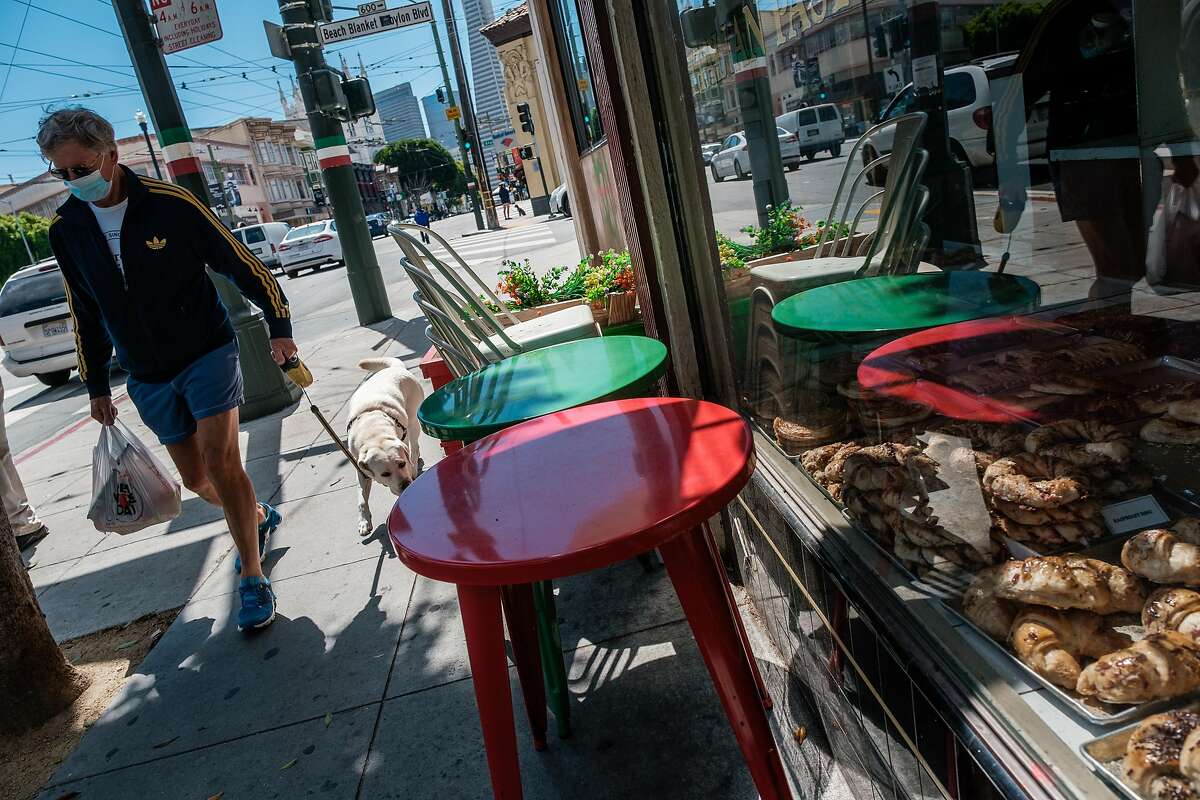 A pedestrian walks past stacked curbside tables and chairs in North Beach in San Francisco on Thursday, May 28, 2020.