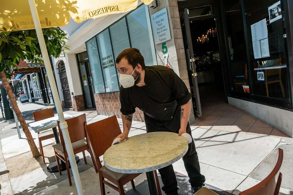 Dylan Boon wipes off tables placed on the sidewalk where patrons can sit at Il Cilentano in North Beach in San Francisco on Thursday, May 28, 2020.