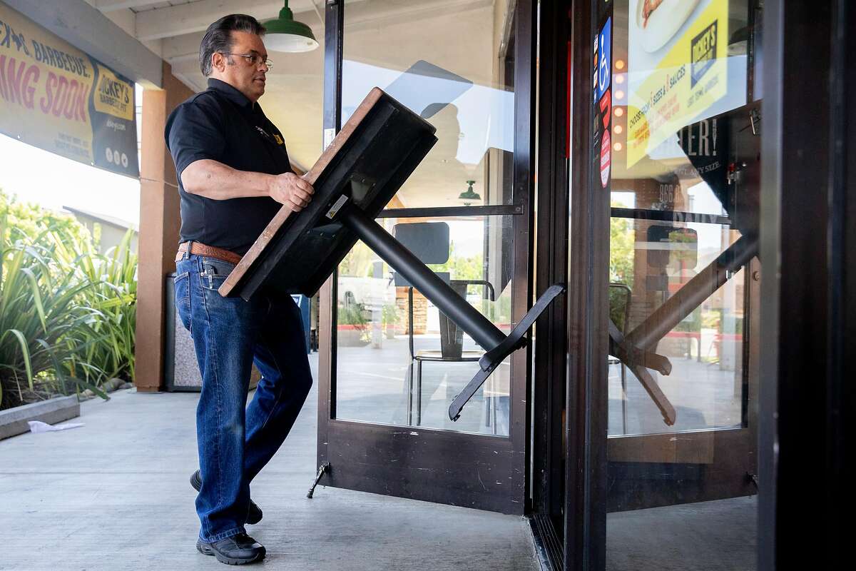 Dickey's Barbecue Pit owner Rene Bassett brings in tables and chairs from outside of his restaurant in Napa, Calif. Tuesday, May 5, 2020. Bassett planned to open his restaurant to in-house and outdoor seating Tuesday but his plans were put on pause by the local health inspector.