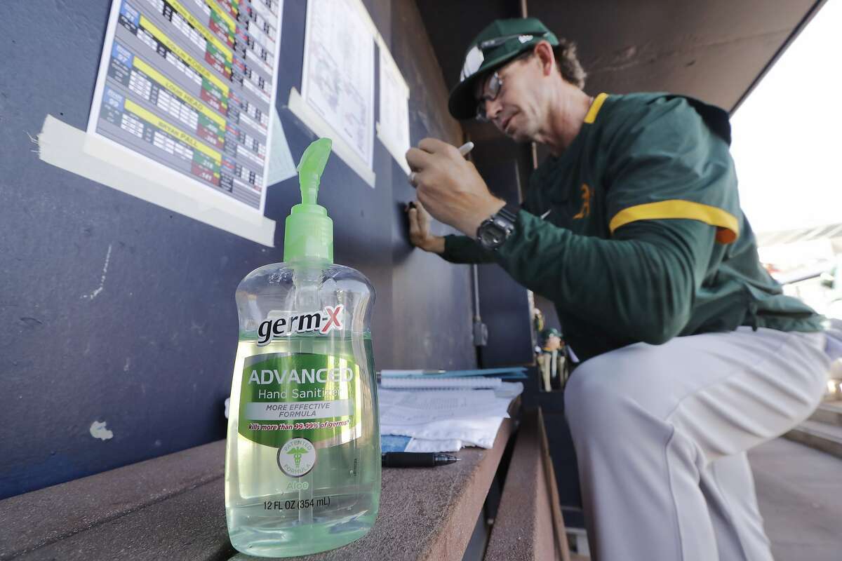 Oakland Athletics minor league manager Scott Steinmann fills-out a line-up in the MLB team's dugout next to a bottle of hand sanitizer before a spring training baseball game against the Seattle Mariners Saturday, March 7, 2020, in Peoria, Ariz. (AP Photo/Elaine Thompson)