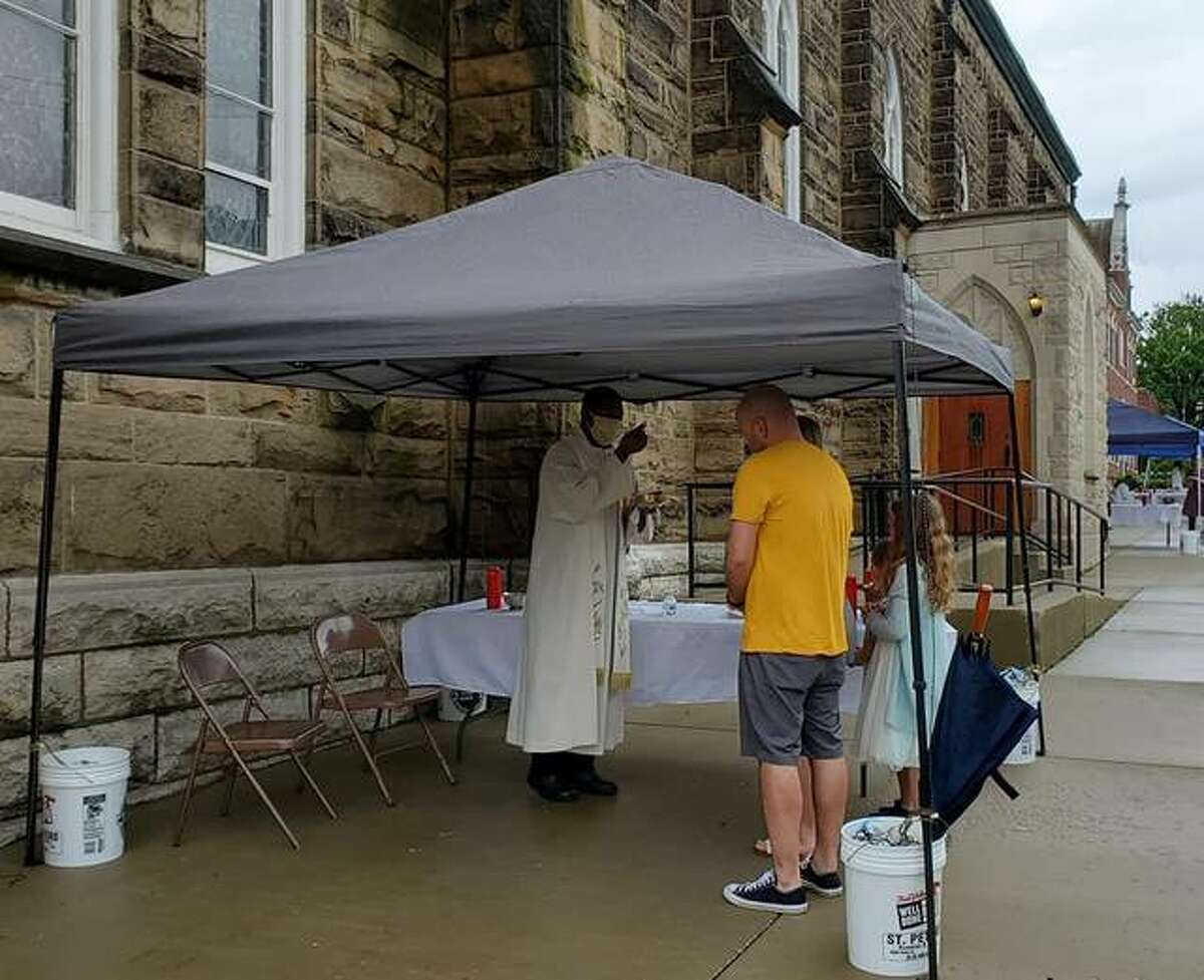 Fr. Benjamin Unachukwu OMV gives Holy Communion to a parish family outside of St. Mary’s Catholic Church in Alton on Sunday, May 17. Gov. J.B. Pritzker announced Thursday that Illinois residents can now attend worship services without fear of prosecution. Bishop Thomas John Paprocki of The Diocese of Springfield has granted permission for public Masses to be celebrated in the diocese as soon as the weekend of June 6-7.